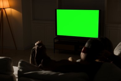 Photo of Couple watching TV on sofa at home in evening, back view