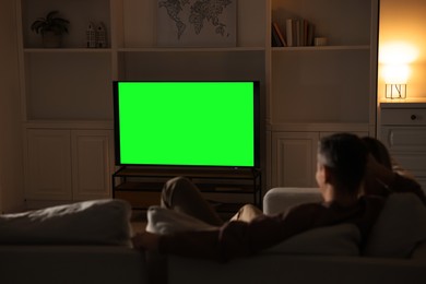 Photo of Couple watching TV on sofa at home in evening, back view