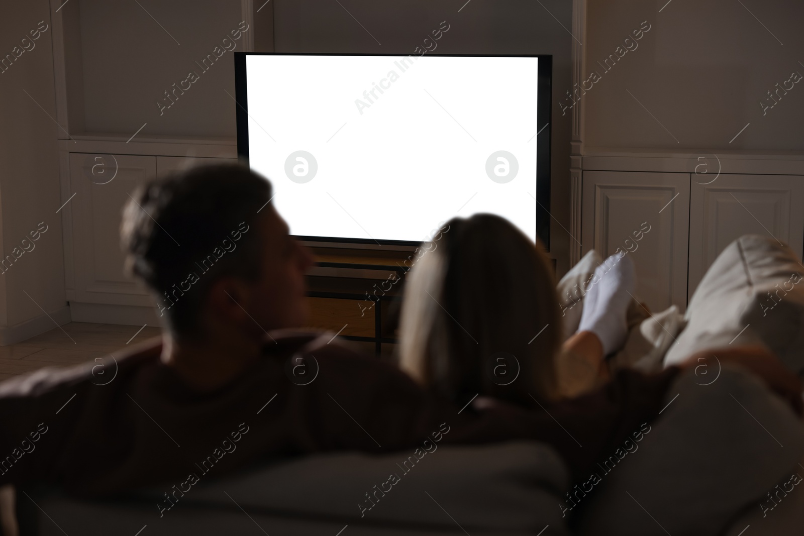 Photo of Couple watching TV on sofa at home in evening