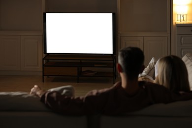 Photo of Couple watching TV on sofa at home in evening, back view