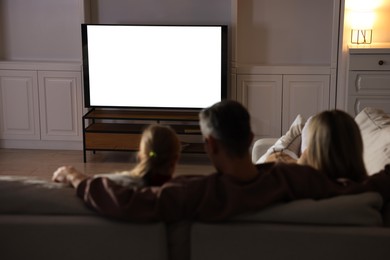 Photo of Family watching TV on sofa at home, back view