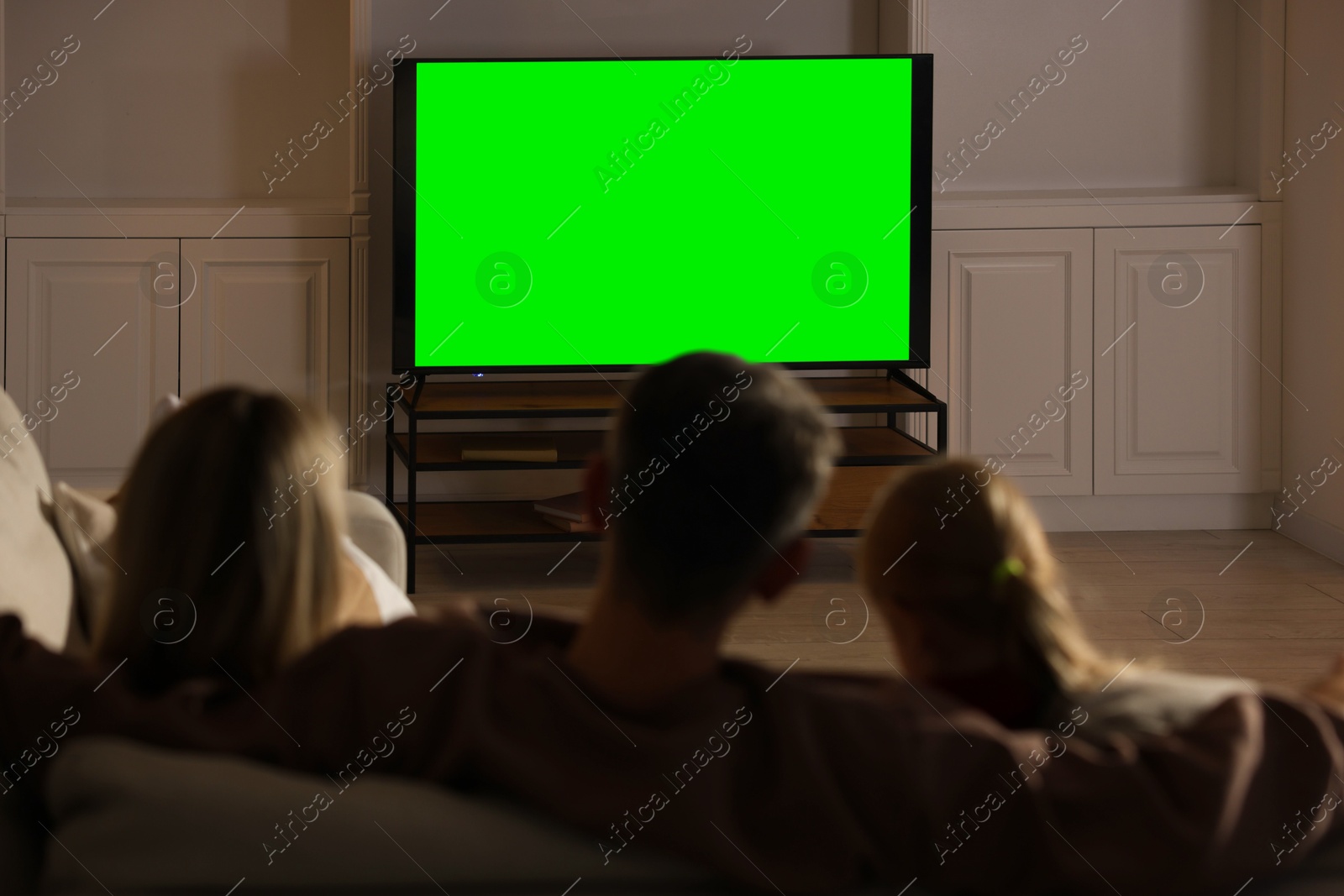 Photo of Family watching TV on sofa at home, back view