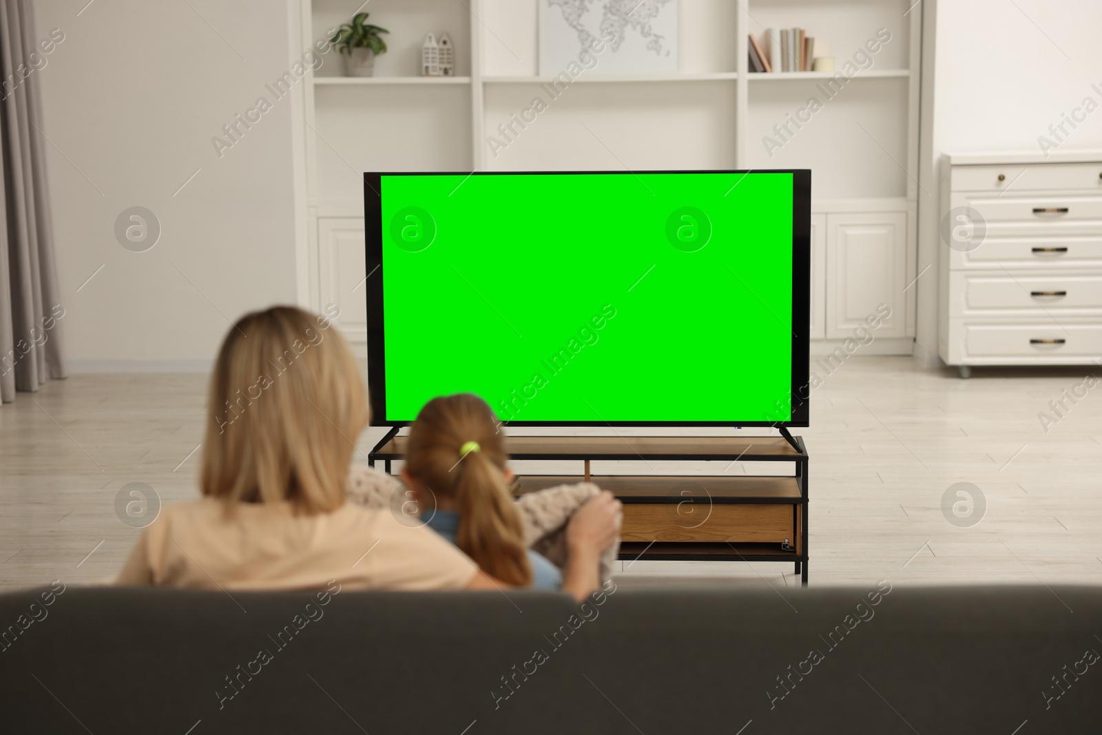 Photo of Mother and her daughter watching TV on sofa at home, back view