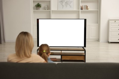 Photo of Mother and her daughter watching TV on sofa at home, back view