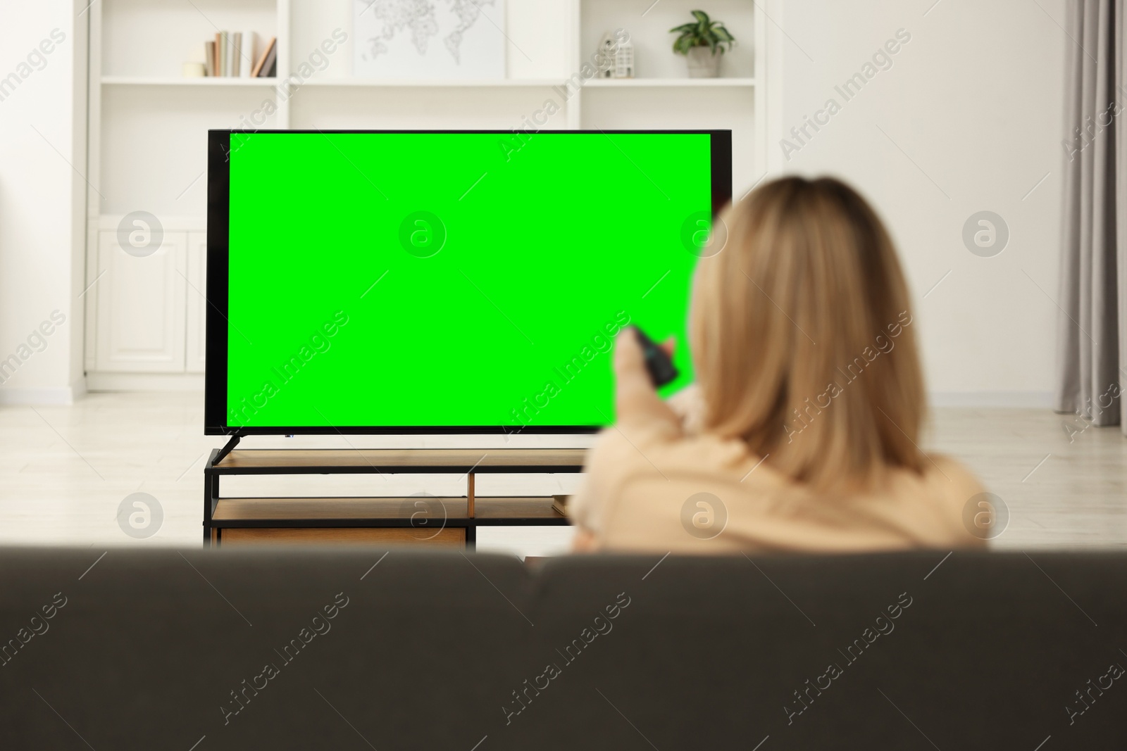 Photo of Woman watching TV on sofa at home, back view