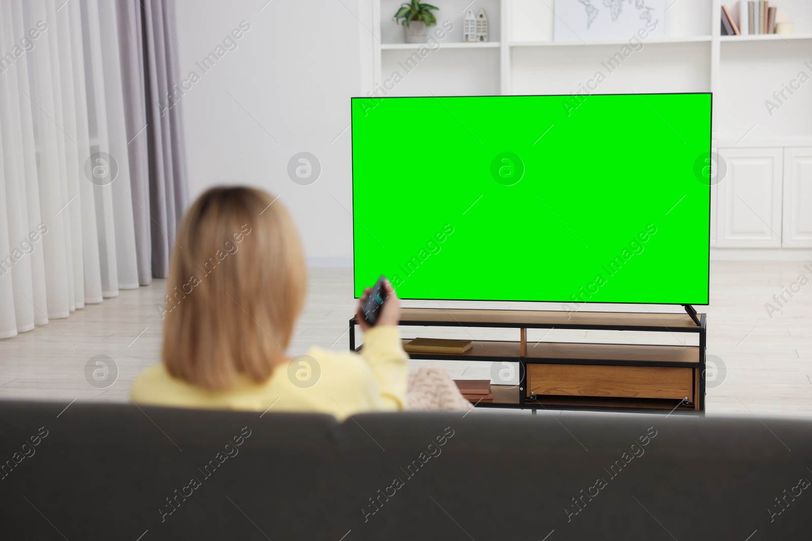 Photo of Woman watching TV on sofa at home, back view