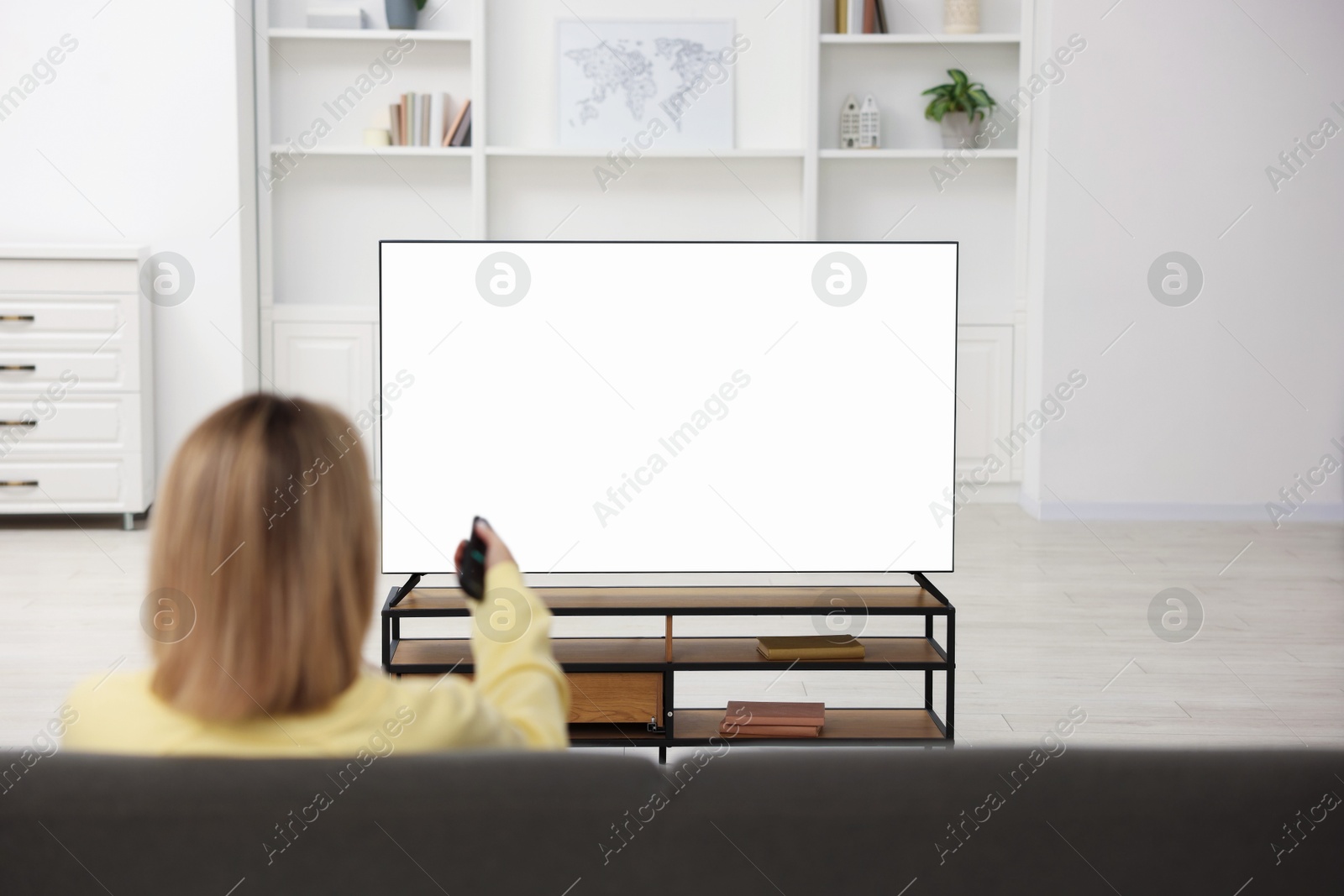 Photo of Woman watching TV on sofa at home, back view