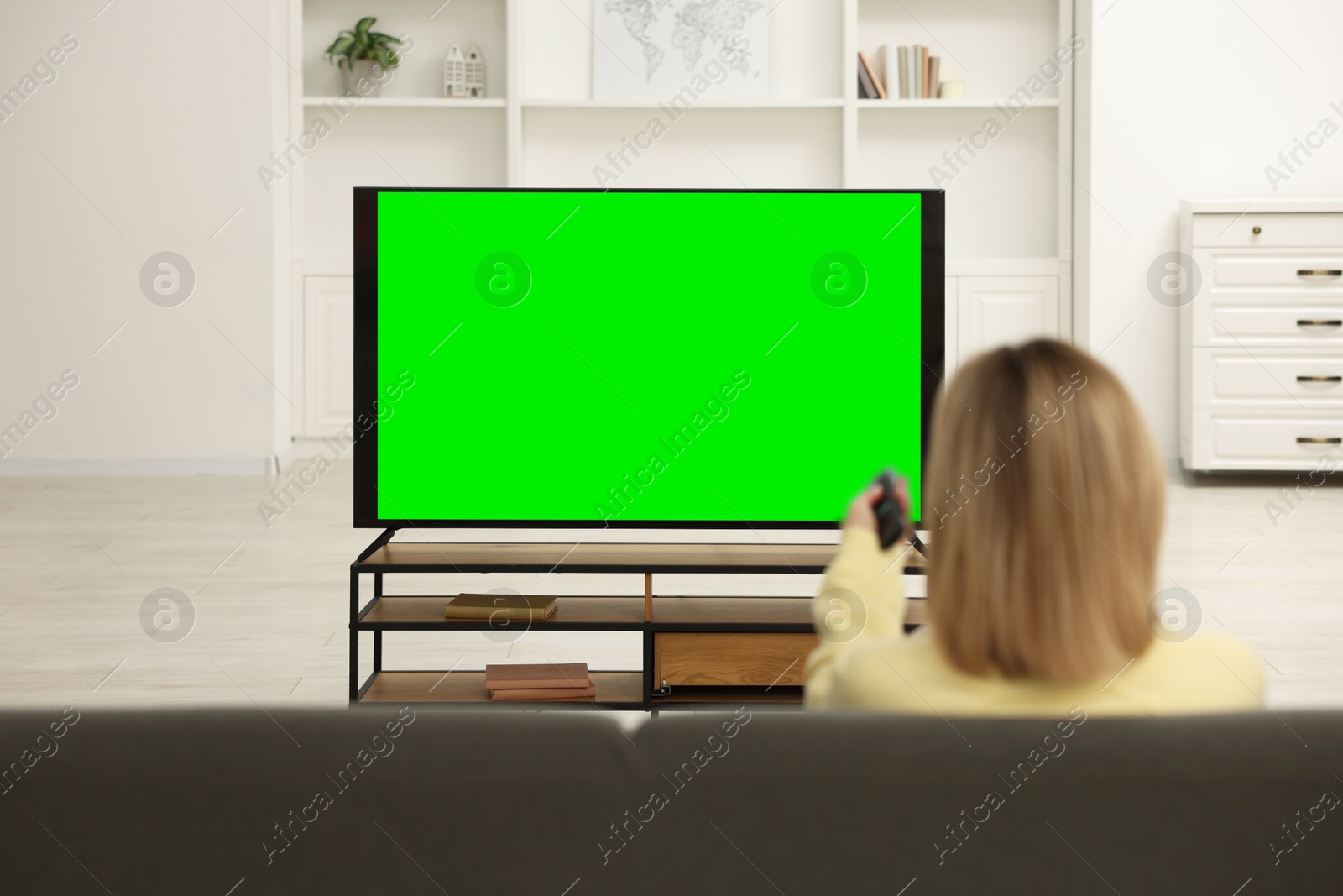 Photo of Woman watching TV on sofa at home, back view