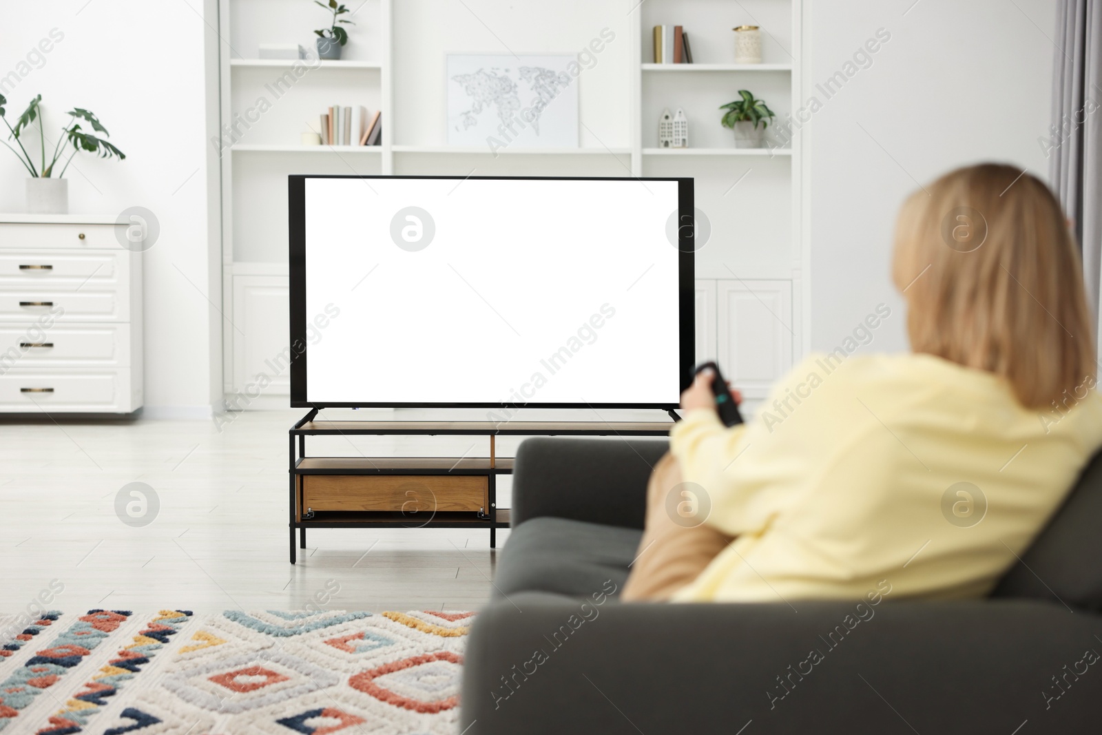 Photo of Woman watching TV on sofa at home, back view