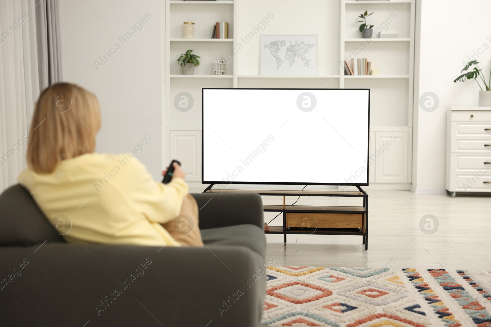 Photo of Woman watching TV on sofa at home, back view