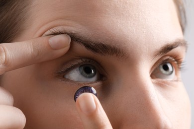 Photo of Woman putting in color contact lens on light background, closeup