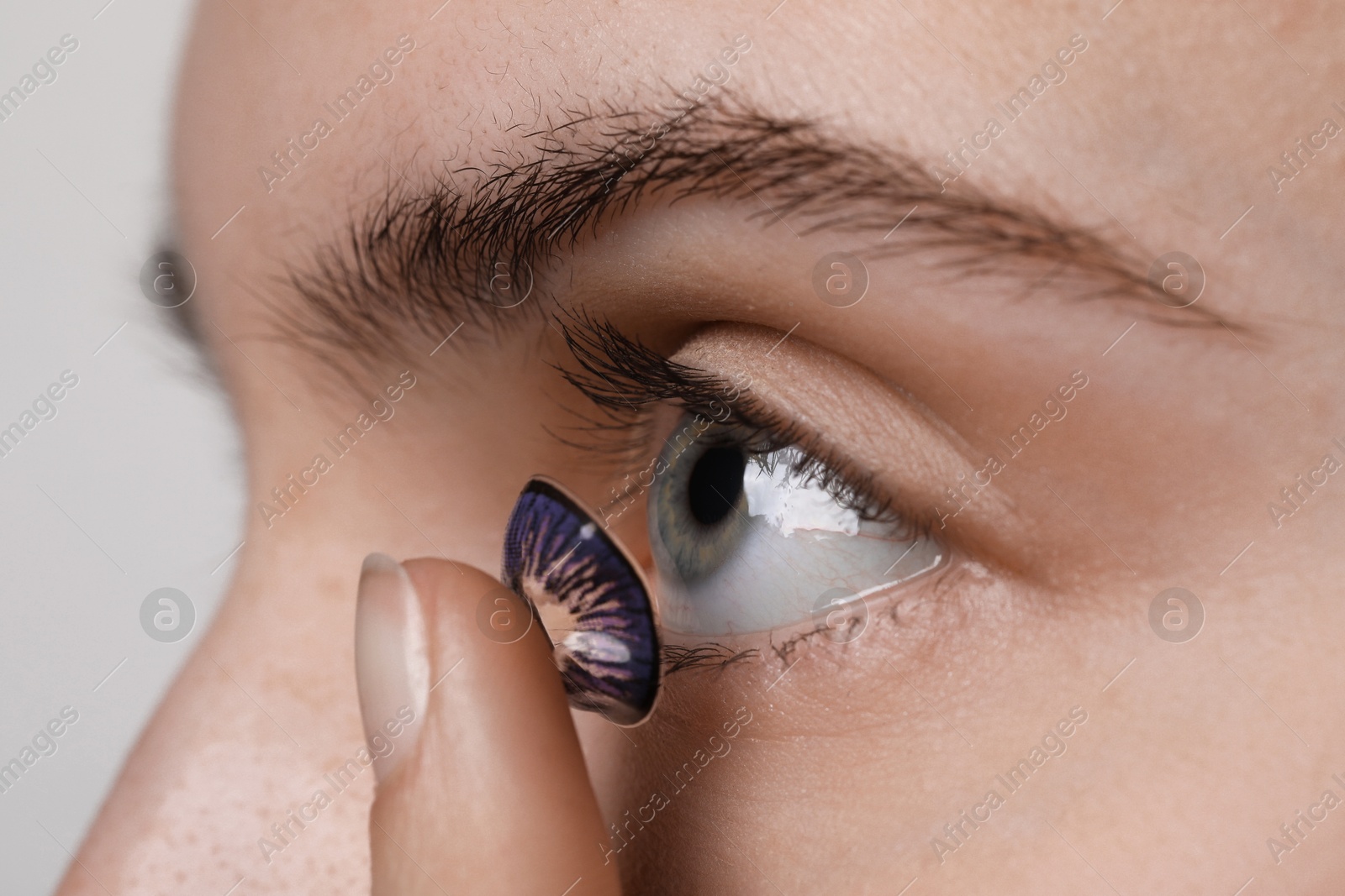 Photo of Woman putting in color contact lens on light background, closeup