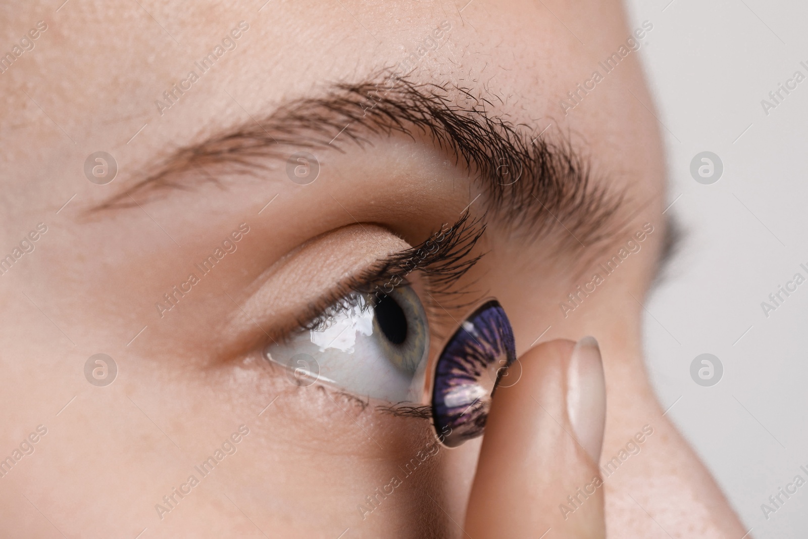 Photo of Woman putting in color contact lens on light background, closeup