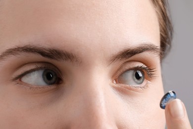 Photo of Woman putting in blue color contact lens on grey background, closeup