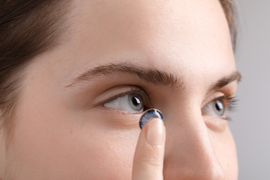 Photo of Woman putting in blue color contact lens on grey background, closeup