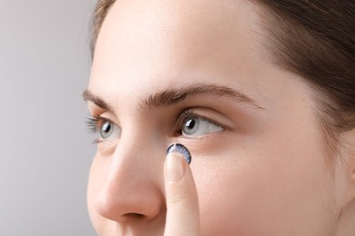 Photo of Woman putting in blue color contact lens on grey background, closeup