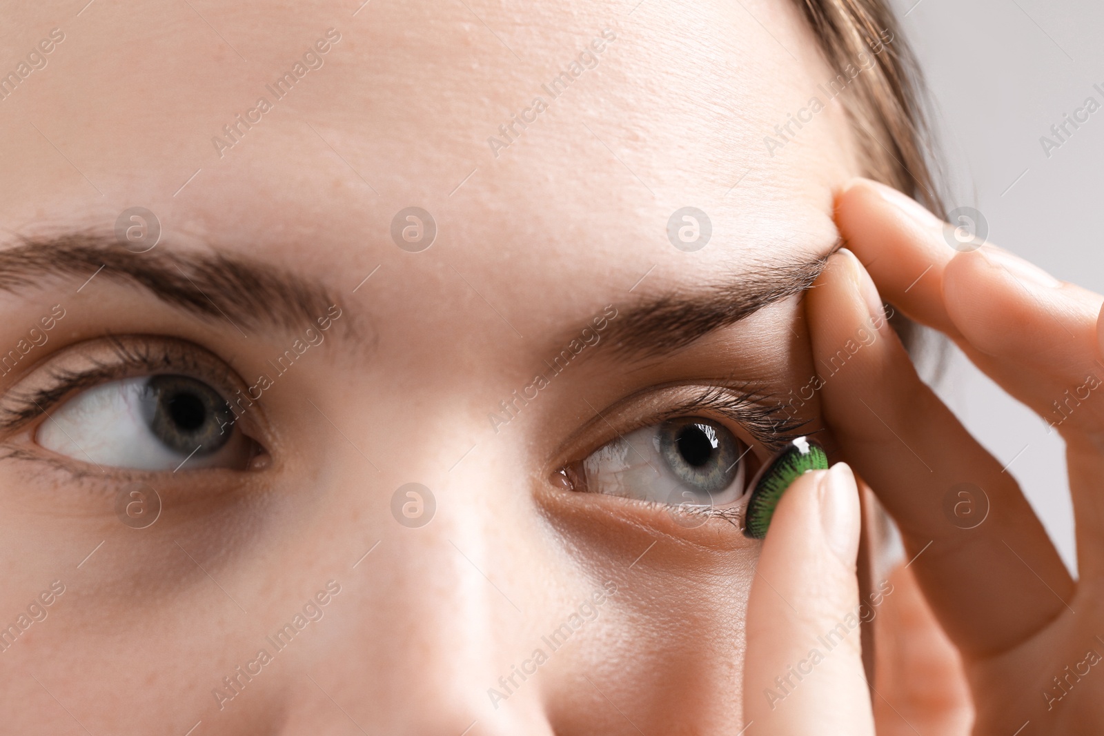 Photo of Woman putting in green color contact lens on grey background, closeup