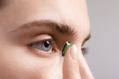 Photo of Woman putting in green color contact lens on grey background, closeup