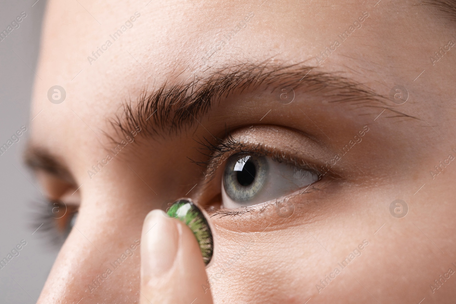 Photo of Woman putting in green color contact lens on grey background, closeup