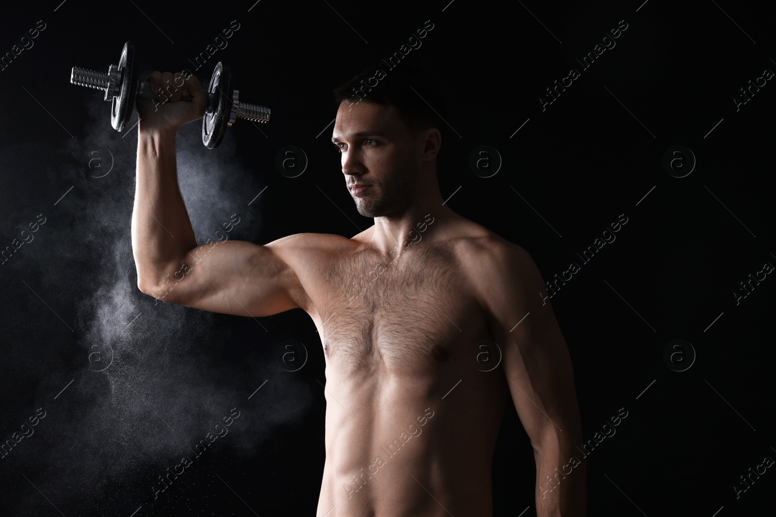 Photo of Man with talcum powder on hand training with barbell against black background