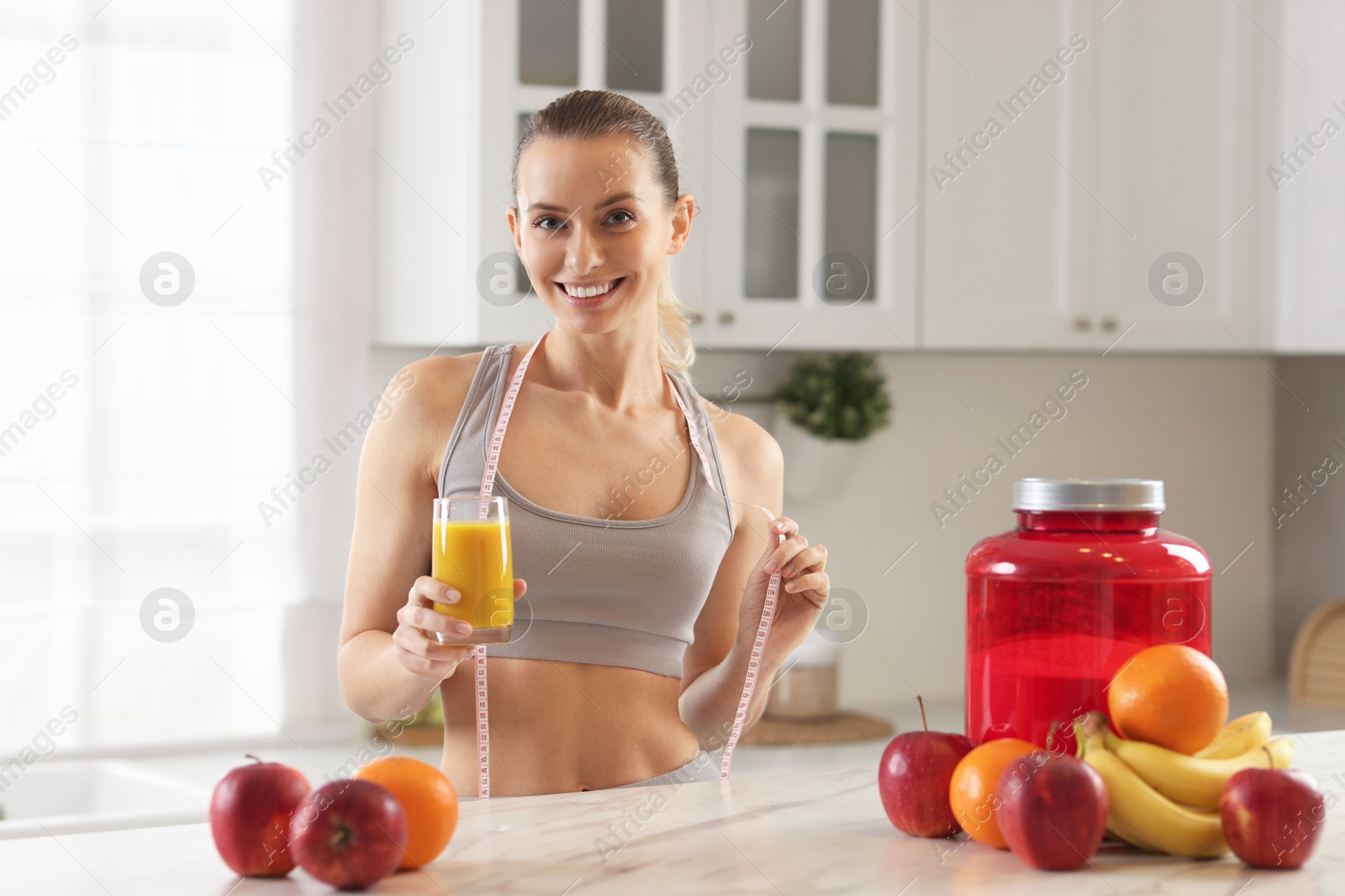 Photo of Weight loss. Happy woman with tasty shake and measuring tape at white marble table in kitchen