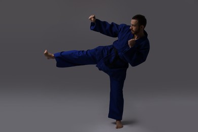 Man in uniform practicing karate on grey background