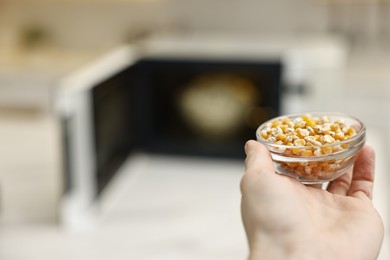 Photo of Woman with bowl of unpopped corn kernels near microwave oven indoors, closeup. Space for text