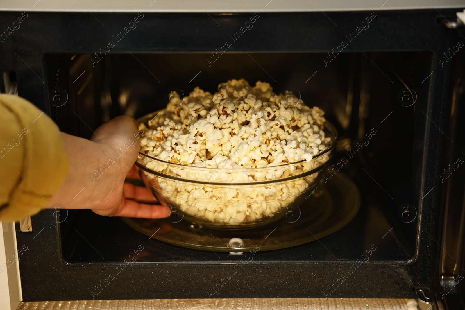 Photo of Woman taking bowl with popcorn out of microwave oven, closeup