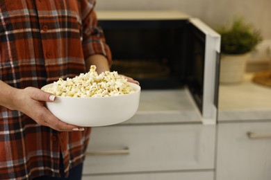 Photo of Woman with bowl of popcorn near microwave oven in kitchen, closeup. Space for text