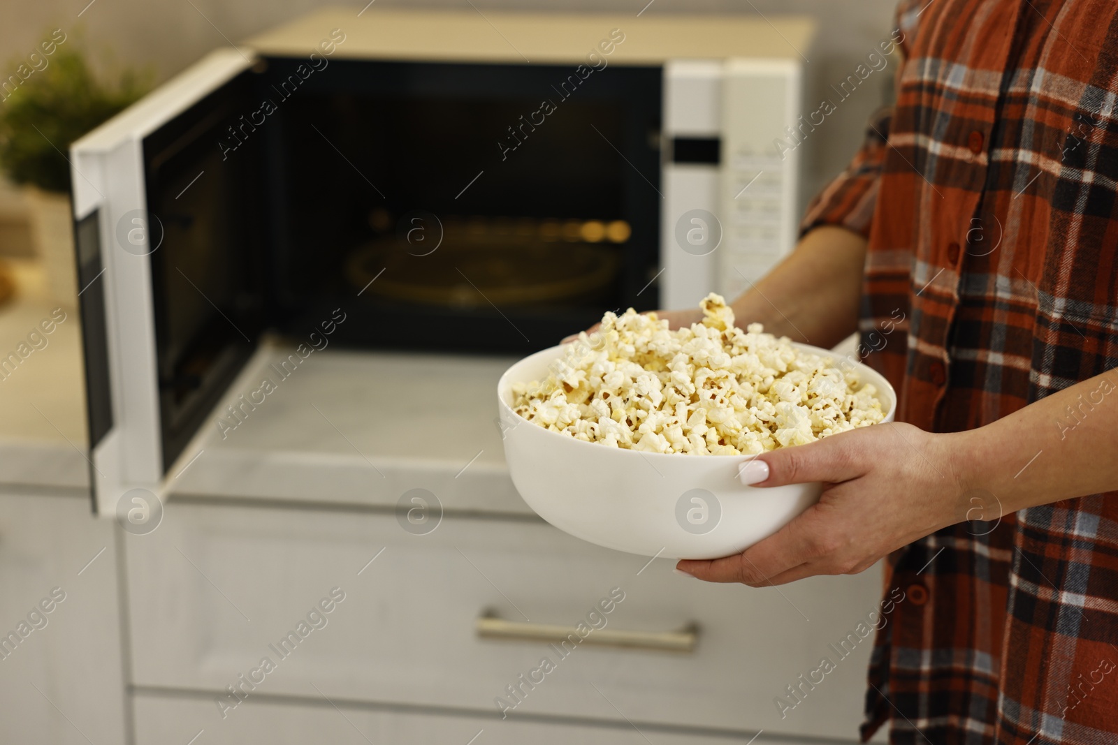 Photo of Woman with bowl of popcorn near microwave oven in kitchen, closeup. Space for text