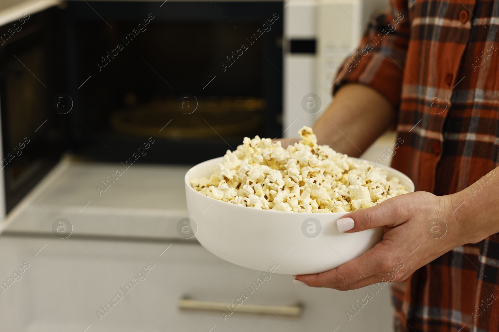 Photo of Woman with bowl of popcorn near microwave oven in kitchen, closeup. Space for text