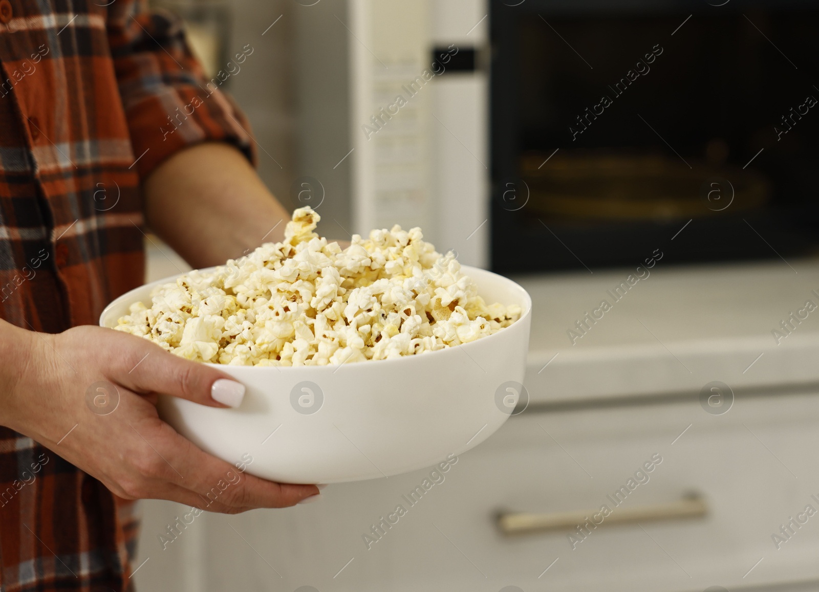 Photo of Woman with bowl of popcorn near microwave oven in kitchen, closeup. Space for text