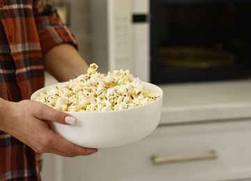 Photo of Woman with bowl of popcorn near microwave oven in kitchen, closeup. Space for text