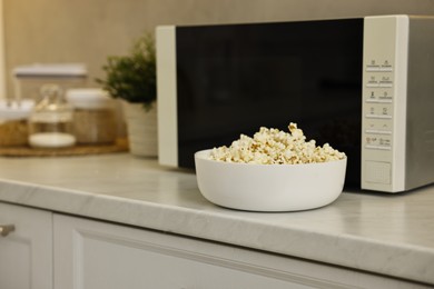 Photo of Bowl of popcorn near microwave oven on white marble countertop in kitchen