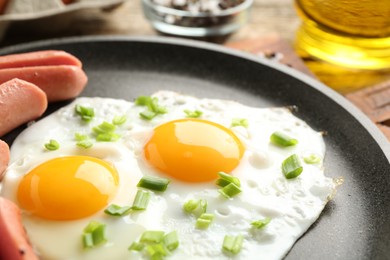 Photo of Tasty fried eggs with cut sausages and green onion in frying pan on table, closeup