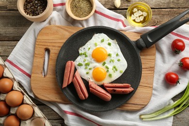 Photo of Tasty fried eggs with cut sausages served on wooden table, flat lay