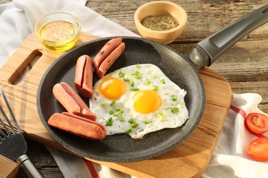 Photo of Tasty fried eggs with cut sausages served on wooden table, closeup