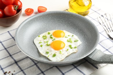 Photo of Tasty fried eggs with green onion in frying pan, oil and tomatoes on table, closeup