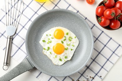 Photo of Tasty fried eggs with green onion in frying pan and tomatoes on white wooden table, flat lay