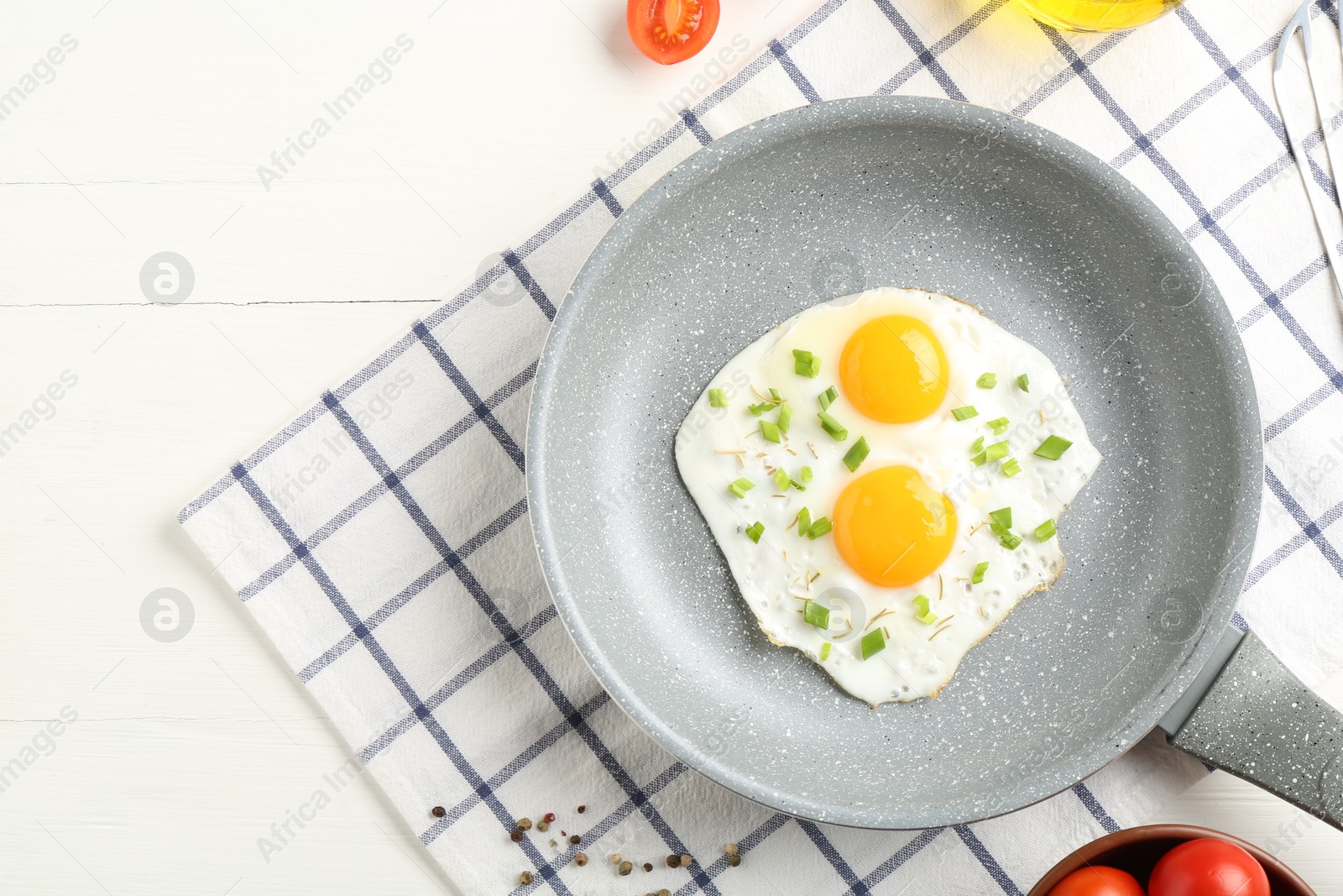 Photo of Tasty fried eggs with green onion in frying pan on white wooden table, top view. Space for text