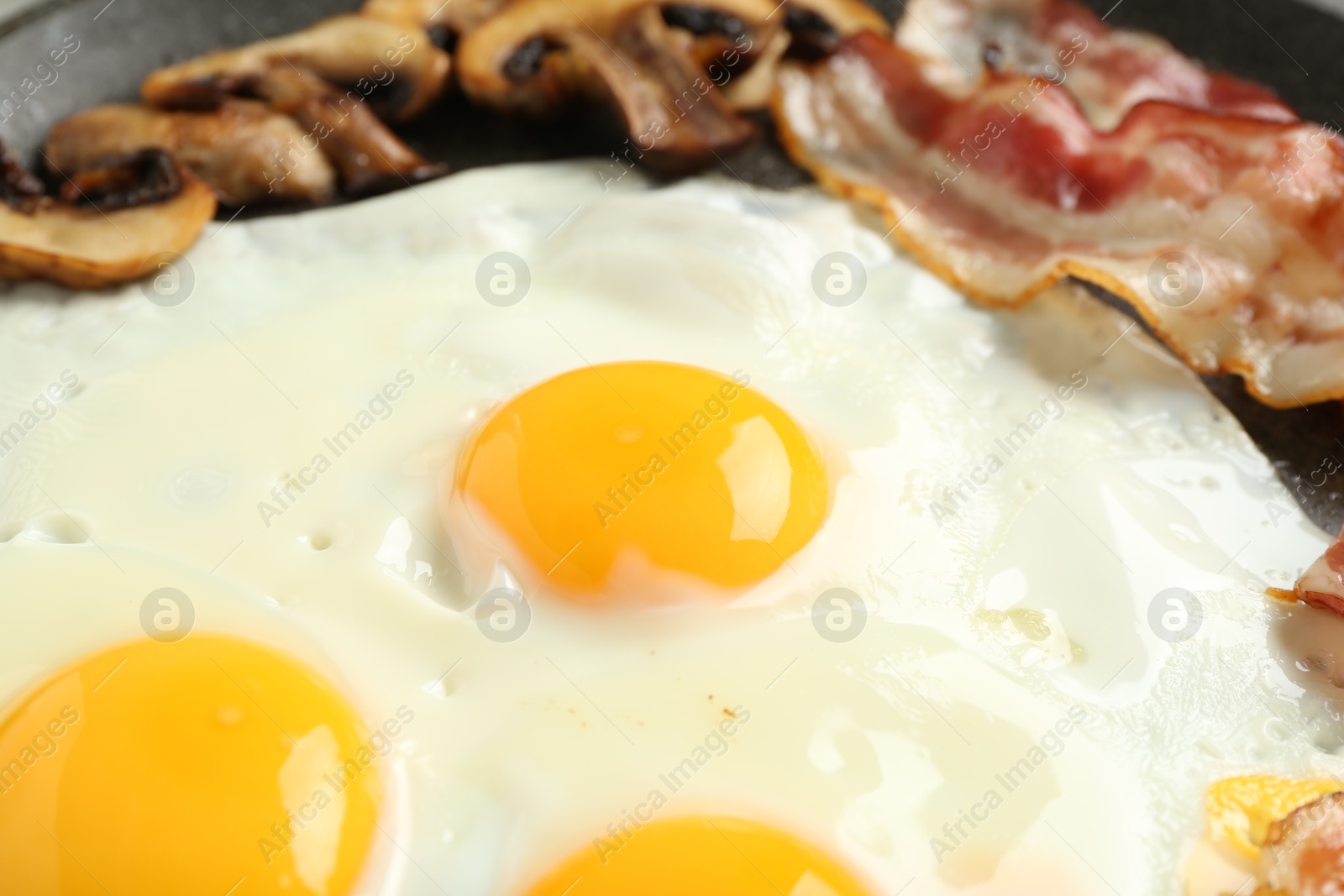 Photo of Tasty fried eggs with bacon and mushrooms in frying pan, closeup