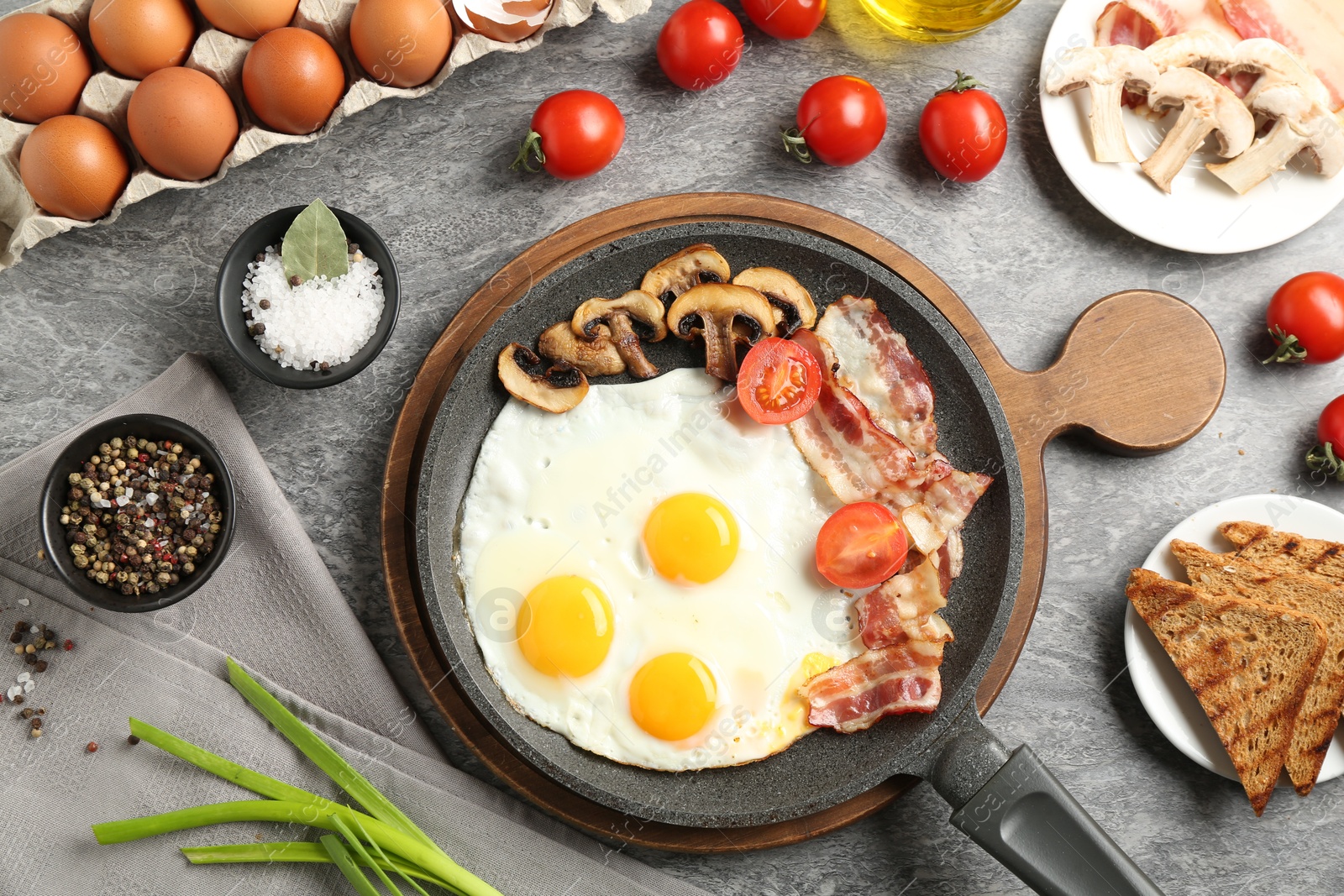 Photo of Tasty fried eggs with bacon and mushrooms served on grey table, flat lay