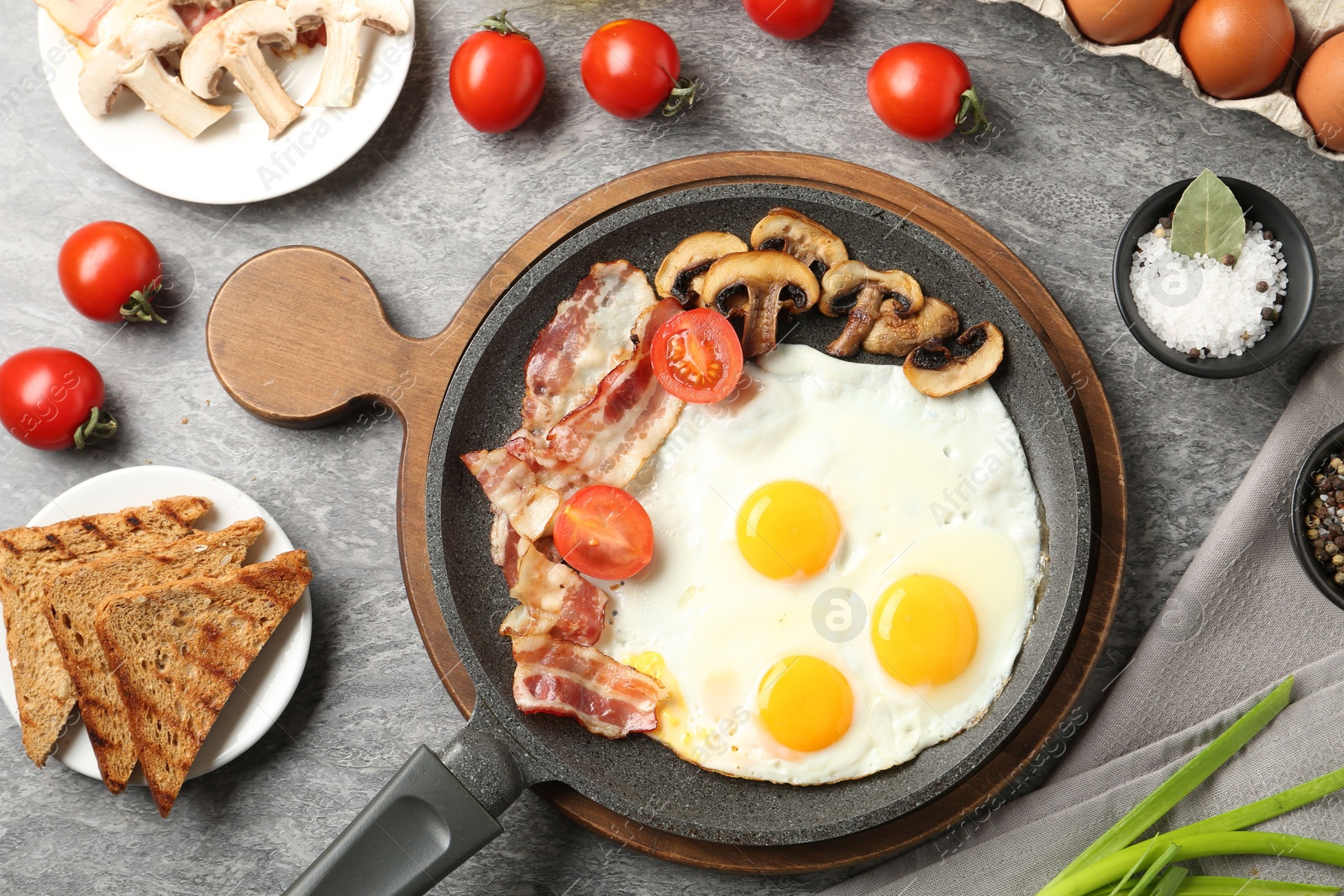 Photo of Tasty fried eggs with bacon and mushrooms served on grey table, flat lay