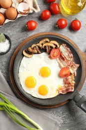 Photo of Tasty fried eggs with bacon and mushrooms served on grey table, flat lay