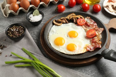 Photo of Tasty fried eggs with bacon and mushrooms served on grey table