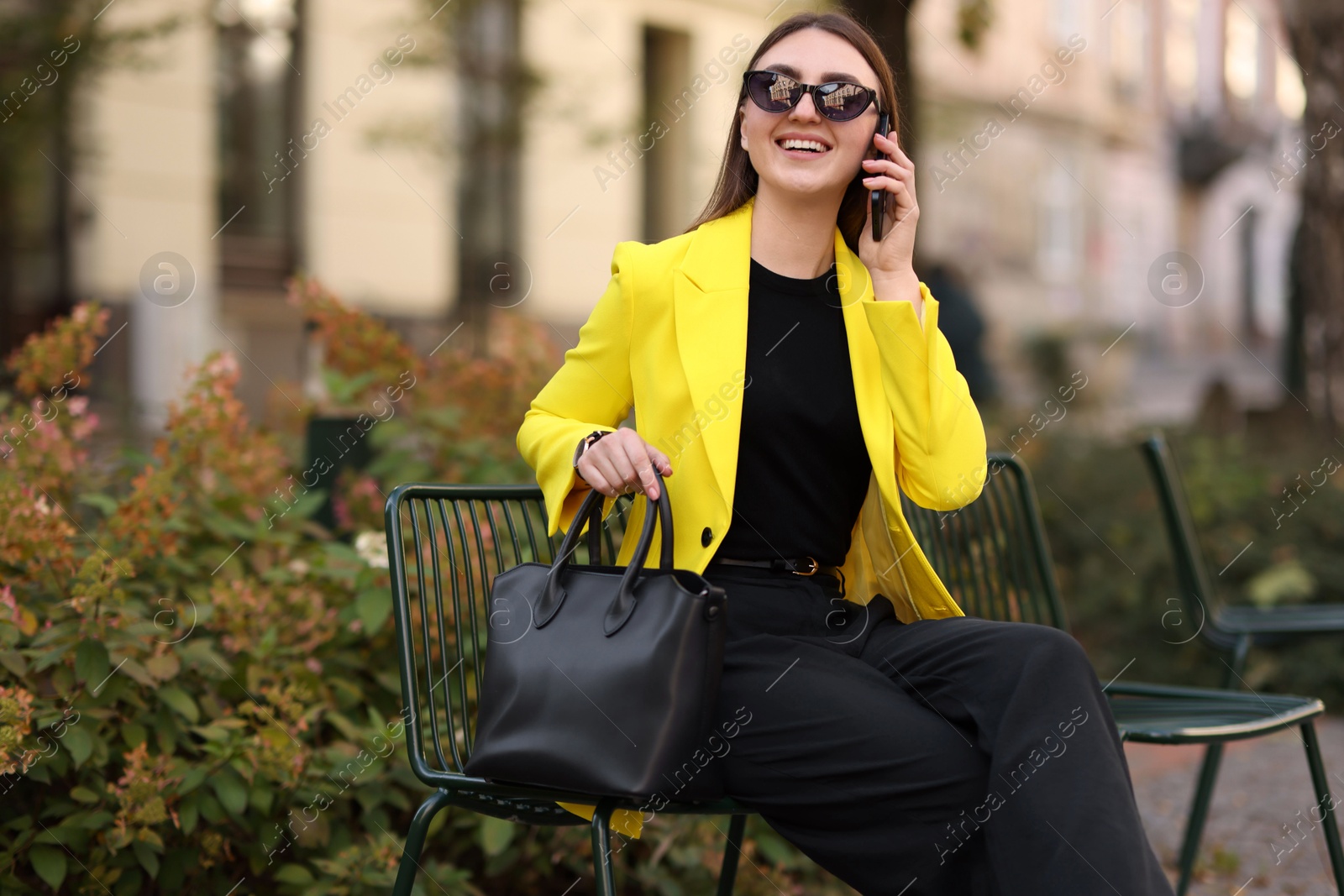 Photo of Smiling businesswoman in stylish suit talking on smartphone outdoors