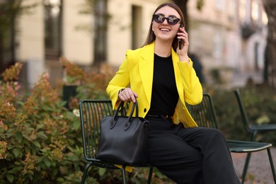 Photo of Smiling businesswoman in stylish suit talking on smartphone outdoors