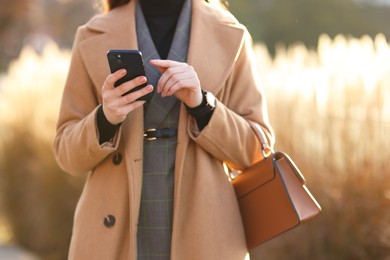 Photo of Businesswoman in stylish suit using smartphone outdoors, closeup