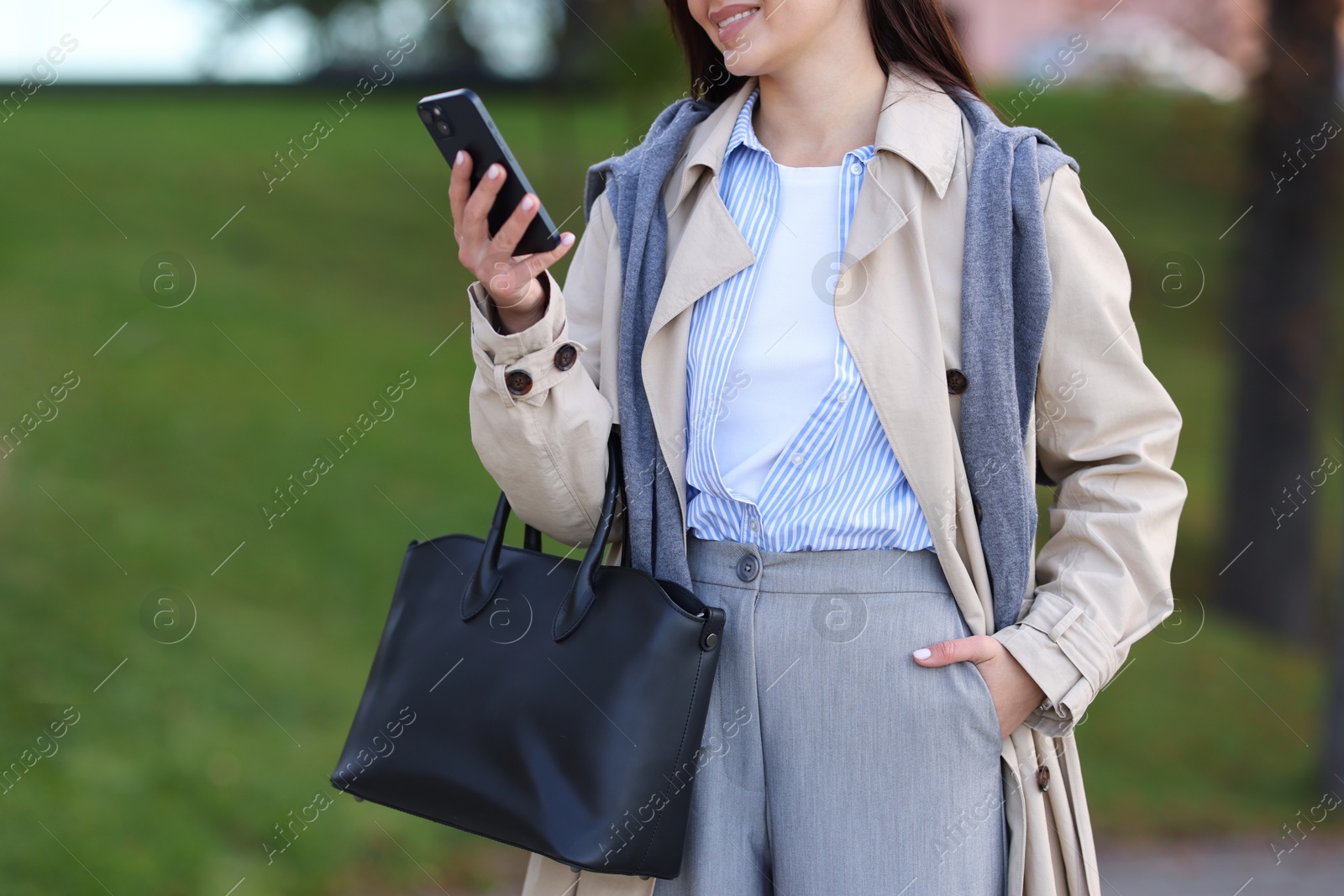 Photo of Smiling businesswoman in stylish suit with smartphone outdoors, closeup. Space for text