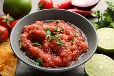 Photo of Delicious spicy salsa sauce in bowl and products on wooden table, closeup